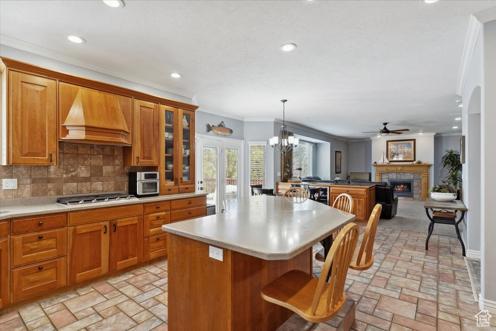 Kitchen featuring premium range hood, ceiling fan, stainless steel gas cooktop, light countertops, and ornamental molding