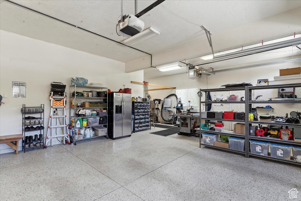 Garage featuring stainless steel refrigerator with ice dispenser, a garage door opener, and a workshop area