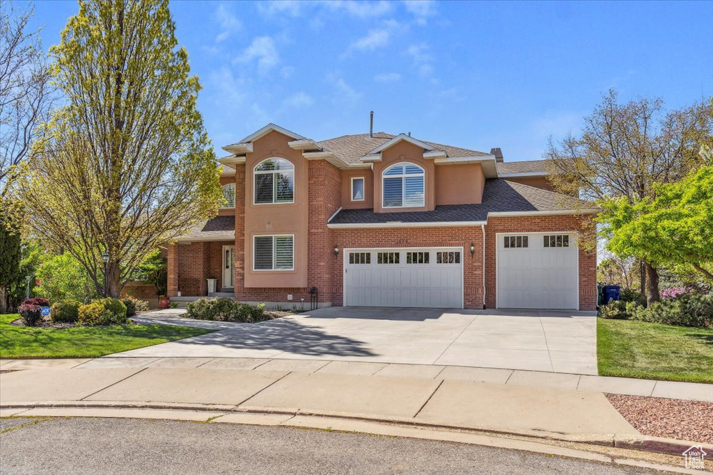 Traditional home featuring concrete driveway, a shingled roof, a front yard, an attached garage, and brick siding