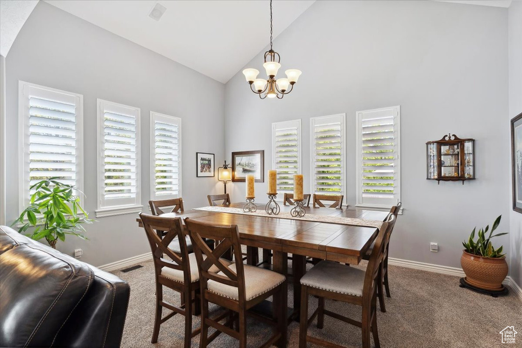 Dining room with carpet flooring, baseboards, a chandelier, and high vaulted ceiling