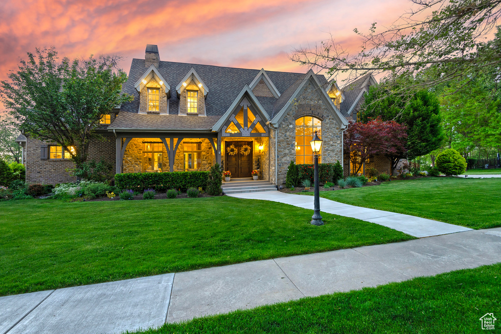 View of front facade with a front yard, a chimney, and stone siding
