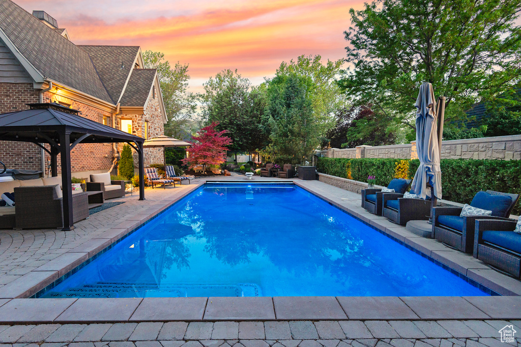 Pool at dusk featuring an outdoor hangout area, a patio area, a gazebo, and a fenced backyard