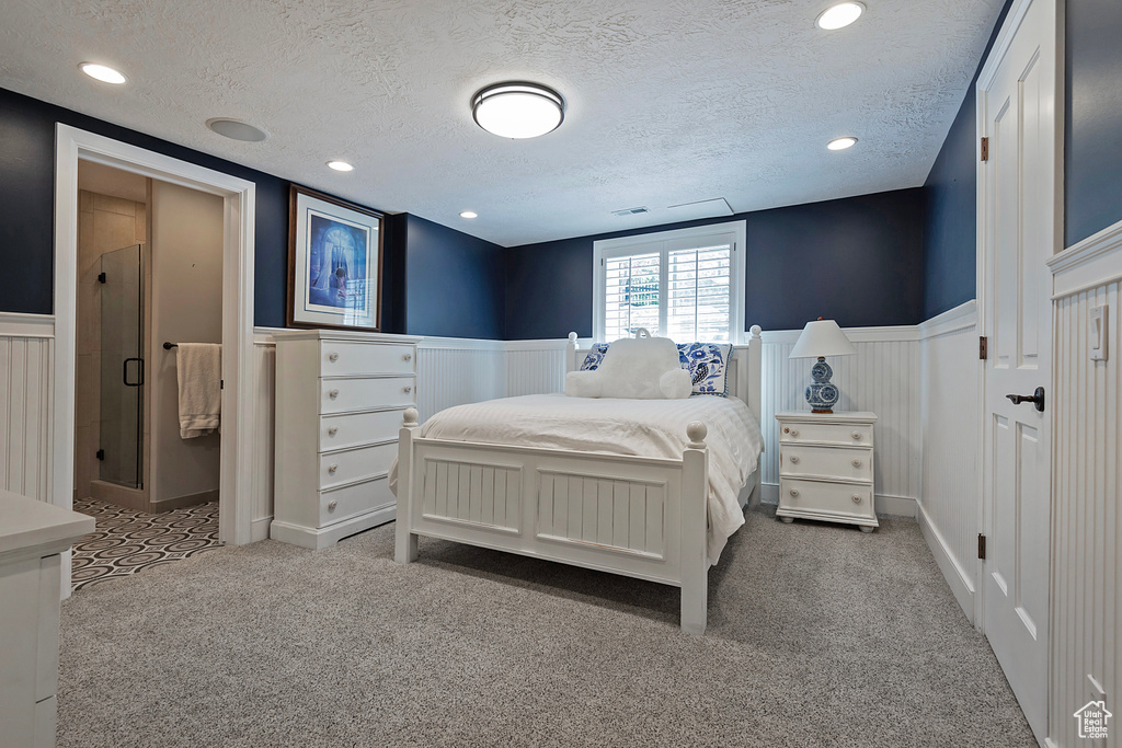 Carpeted bedroom with wainscoting, a textured ceiling, and a decorative wall