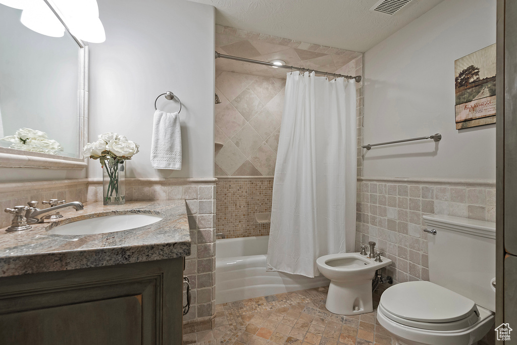 Bathroom featuring vanity, toilet, shower / bath combo with shower curtain, a bidet, and tile walls