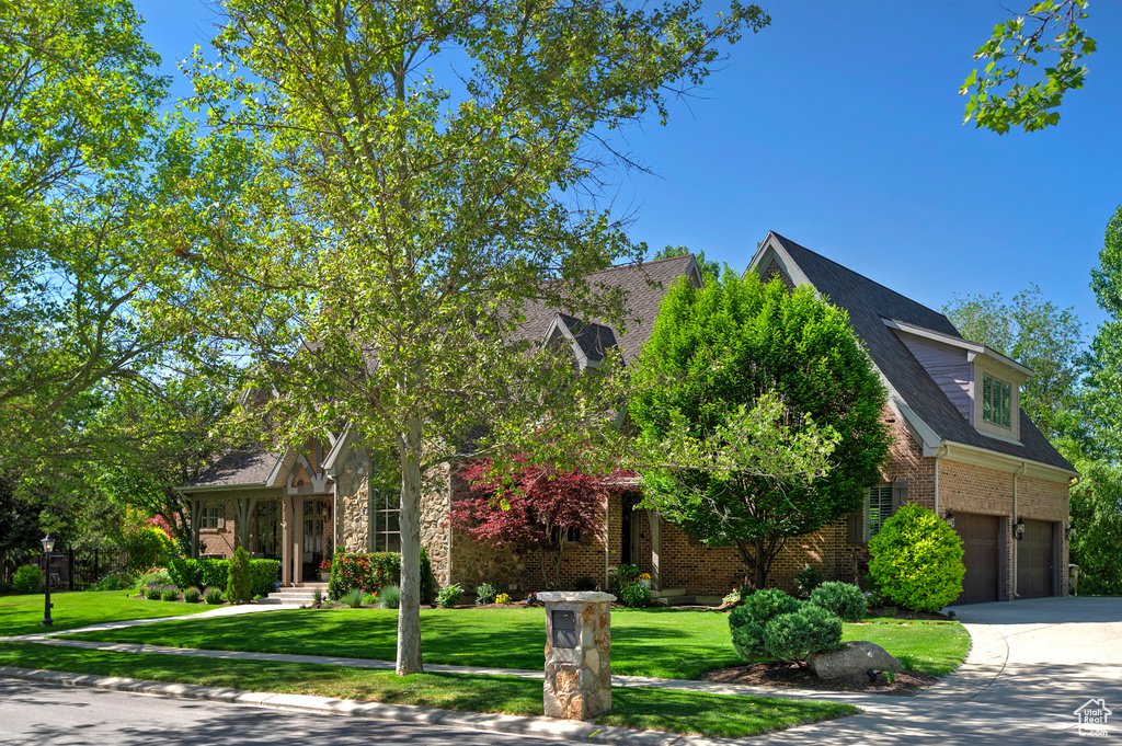 View of property hidden behind natural elements with brick siding, driveway, a garage, and a front lawn