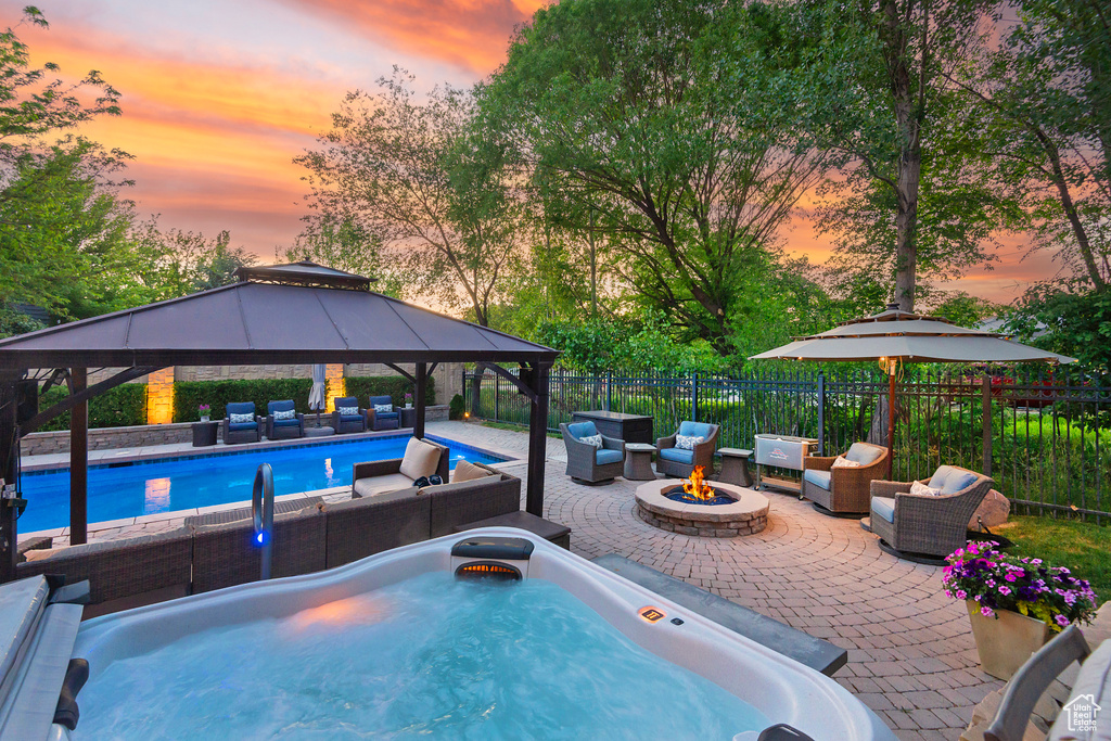 Pool at dusk with an outdoor living space with a fire pit, a gazebo, a patio, and a hot tub