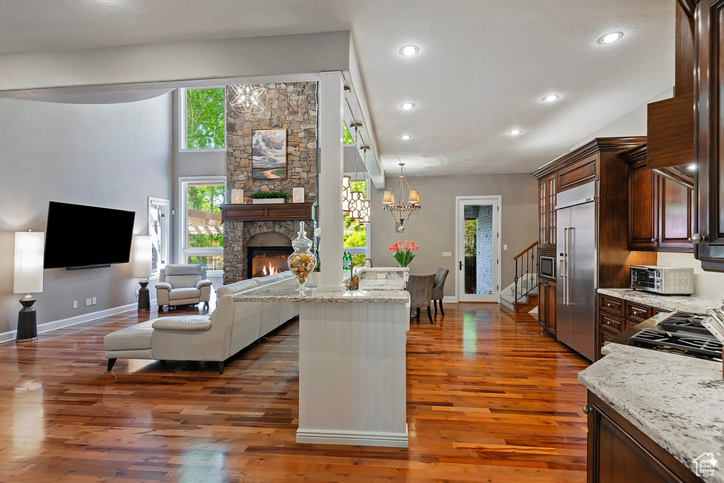 Living room with baseboards, wood finished floors, a stone fireplace, stairs, and recessed lighting