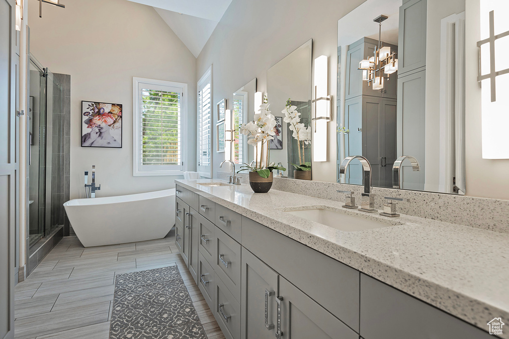 Bathroom with double vanity, a soaking tub, a chandelier, a stall shower, and vaulted ceiling