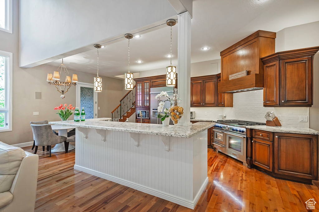 Kitchen with high quality appliances, a breakfast bar, baseboards, light wood-type flooring, and decorative backsplash