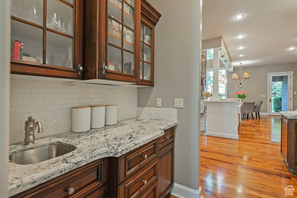 Kitchen with a sink, light wood finished floors, backsplash, light stone countertops, and glass insert cabinets