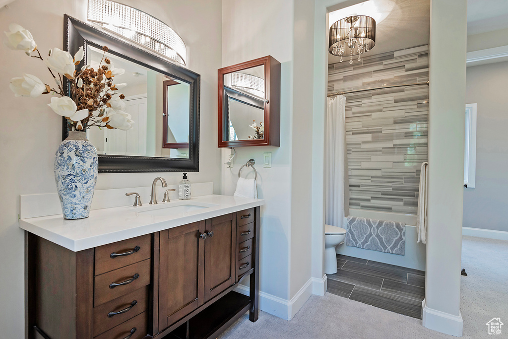 Bathroom featuring vanity, toilet, a chandelier, baseboards, and shower / bath combo with shower curtain