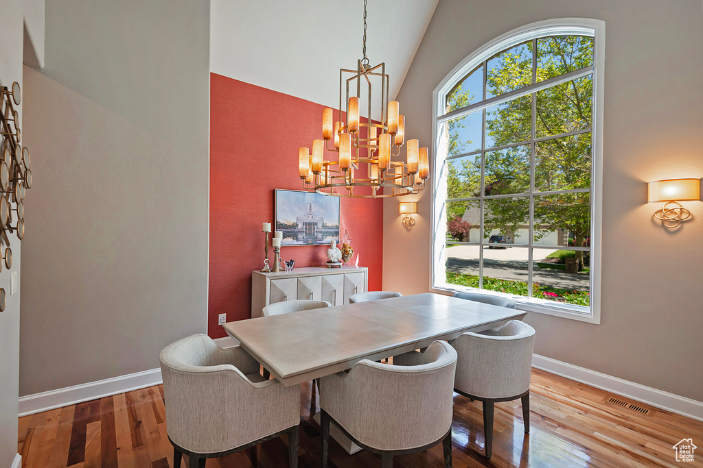 Dining space featuring a chandelier, wood finished floors, baseboards, and high vaulted ceiling
