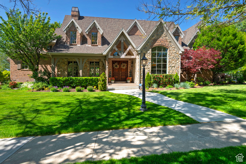 View of front of home featuring stone siding, a front yard, and a chimney