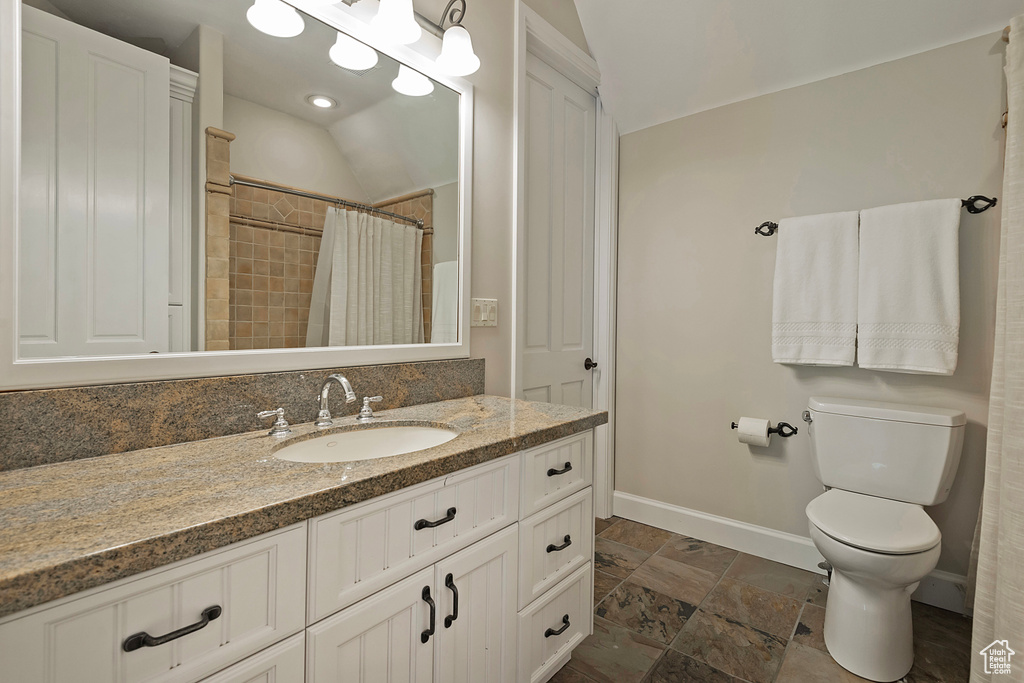 Full bathroom featuring baseboards, vanity, toilet, lofted ceiling, and stone finish flooring