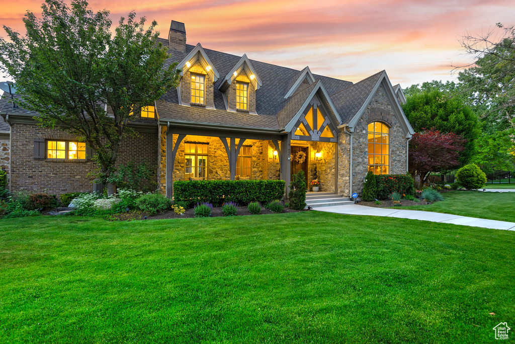 View of front of house featuring a lawn, a chimney, brick siding, roof with shingles, and stone siding