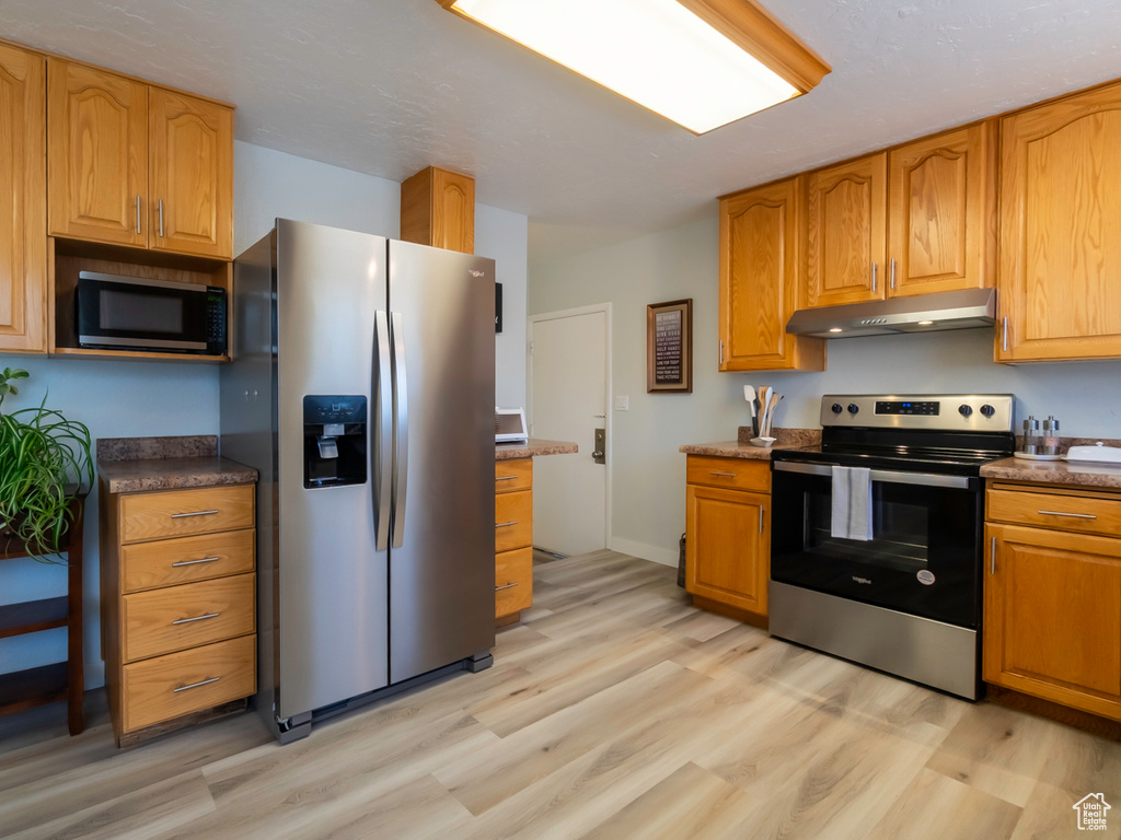 Kitchen with stainless steel appliances, under cabinet range hood, light wood-type flooring, and brown cabinetry
