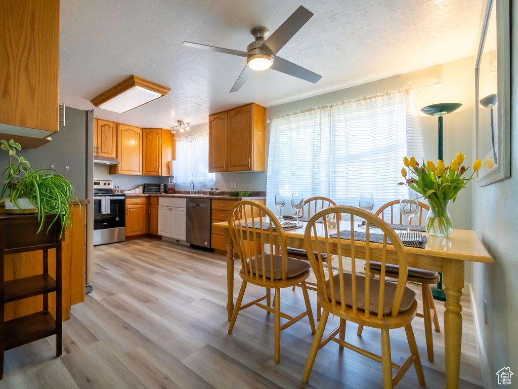 Kitchen with stainless steel appliances, a ceiling fan, light wood-style floors, and under cabinet range hood