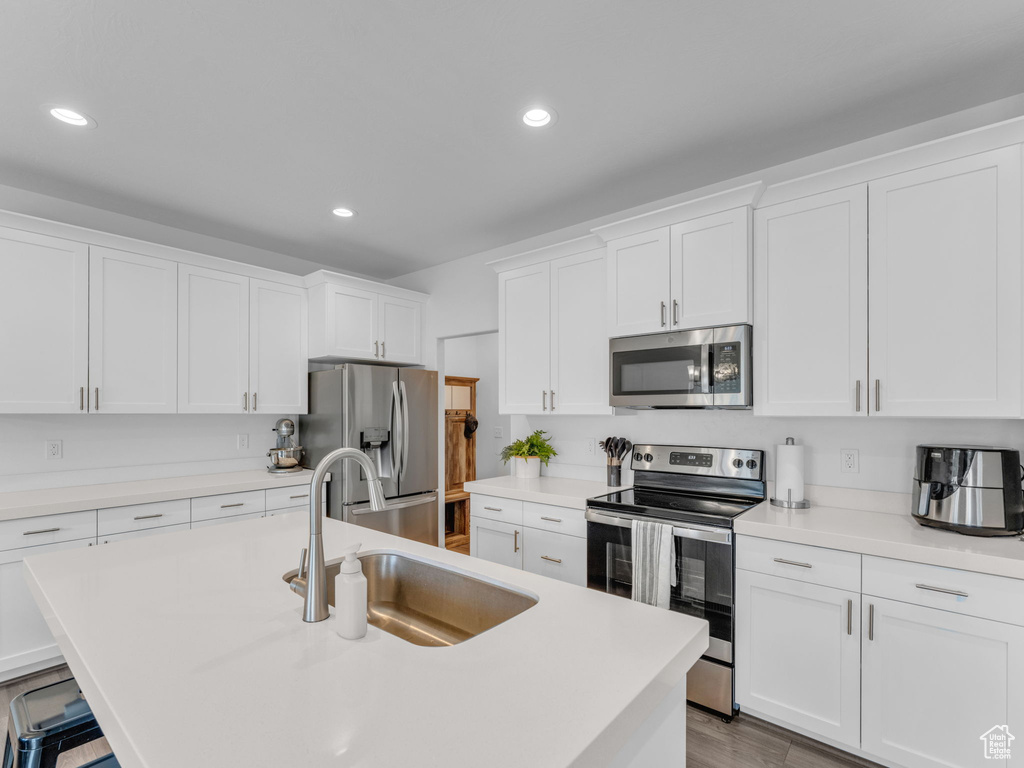 Kitchen with stainless steel appliances, a sink, white cabinetry, recessed lighting, and a kitchen island with sink
