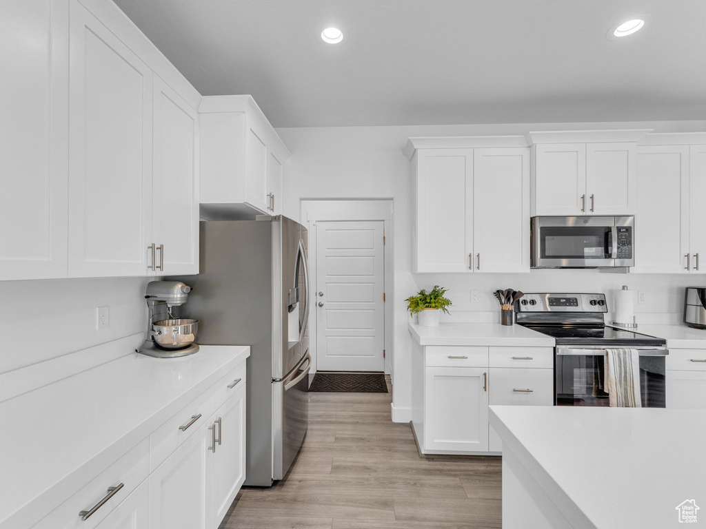 Kitchen with stainless steel appliances, recessed lighting, light countertops, white cabinetry, and light wood-type flooring