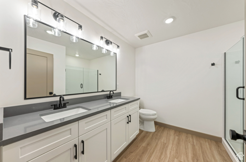 Full bath featuring double vanity, wood finished floors, a shower stall, toilet, and baseboards