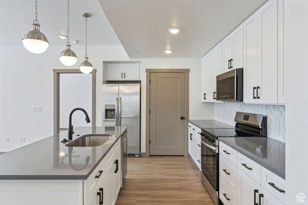 Kitchen featuring appliances with stainless steel finishes, a sink, dark countertops, light wood-style flooring, and tasteful backsplash