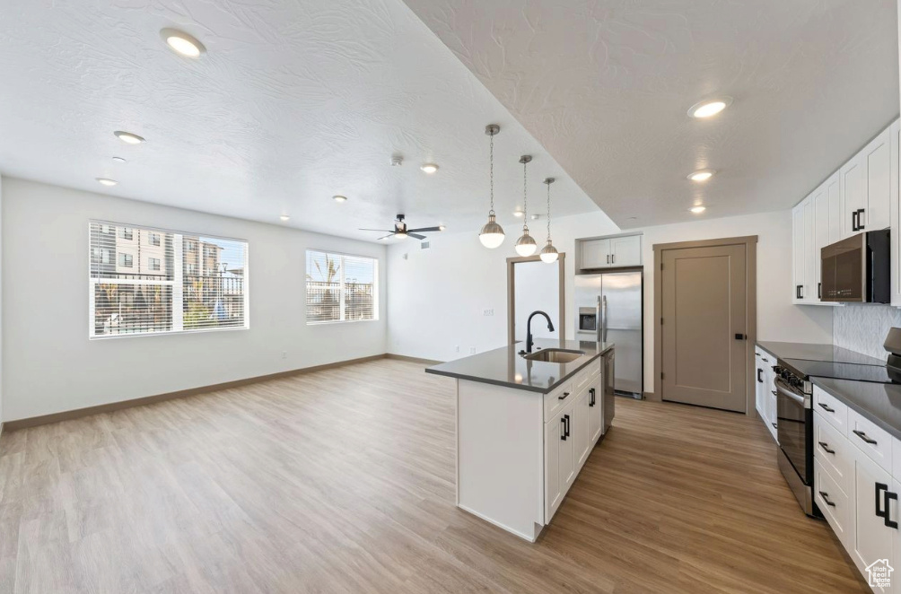 Kitchen featuring stainless steel appliances, dark countertops, a sink, light wood-type flooring, and a center island with sink