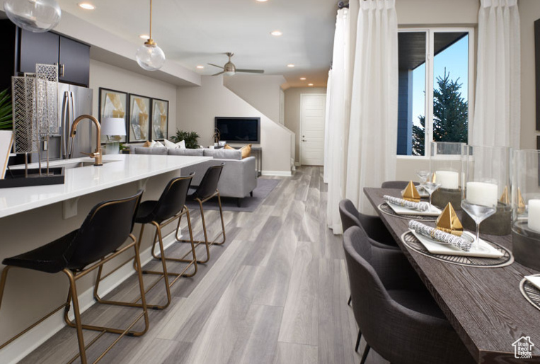Kitchen featuring a ceiling fan, light wood-type flooring, stainless steel fridge, recessed lighting, and a breakfast bar