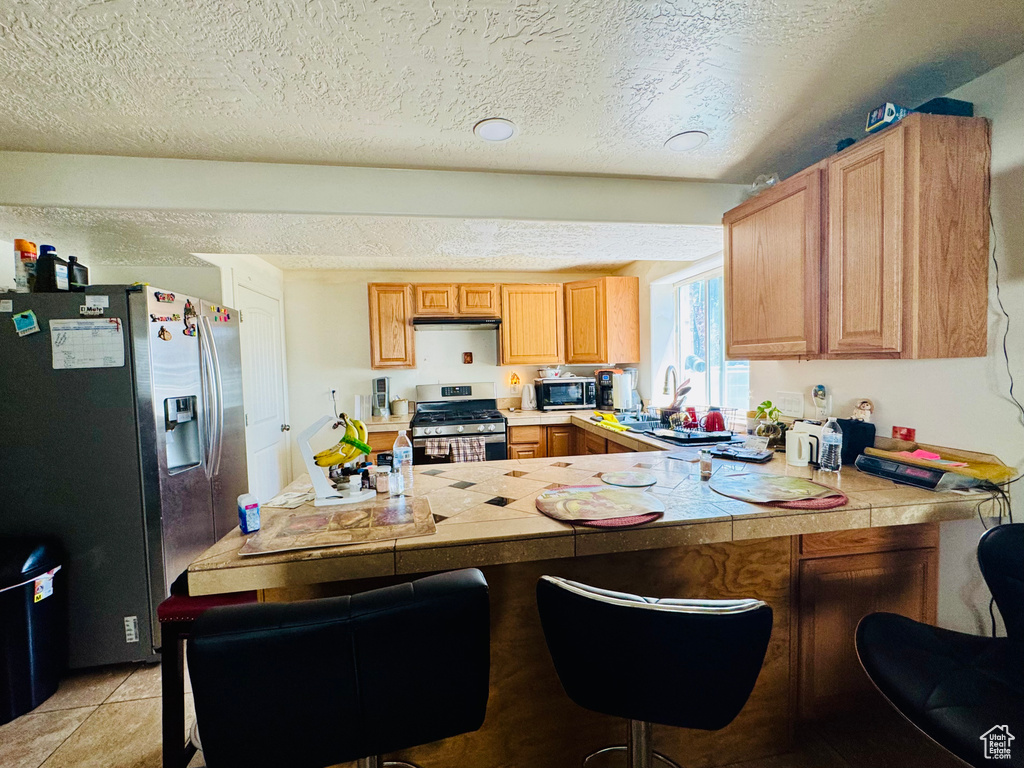 Kitchen with appliances with stainless steel finishes, a peninsula, a kitchen bar, a sink, and a textured ceiling