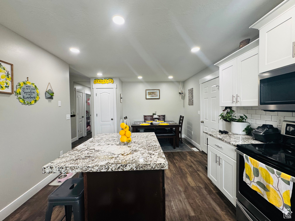 Kitchen with appliances with stainless steel finishes, baseboards, a kitchen island, white cabinets, and recessed lighting
