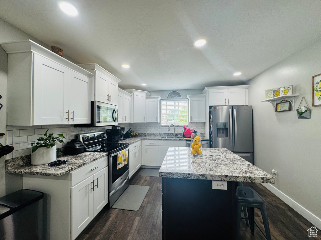 Kitchen with appliances with stainless steel finishes, a sink, a kitchen island, a breakfast bar area, and decorative backsplash