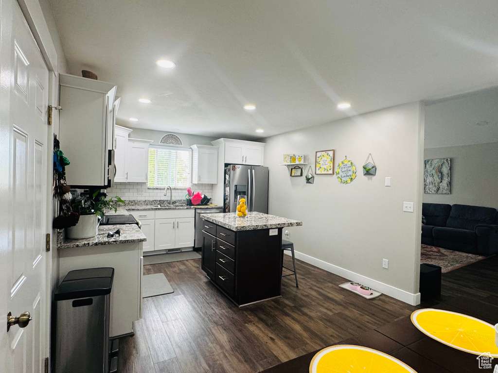 Kitchen with appliances with stainless steel finishes, dark wood-style flooring, a breakfast bar, a kitchen island, and white cabinets