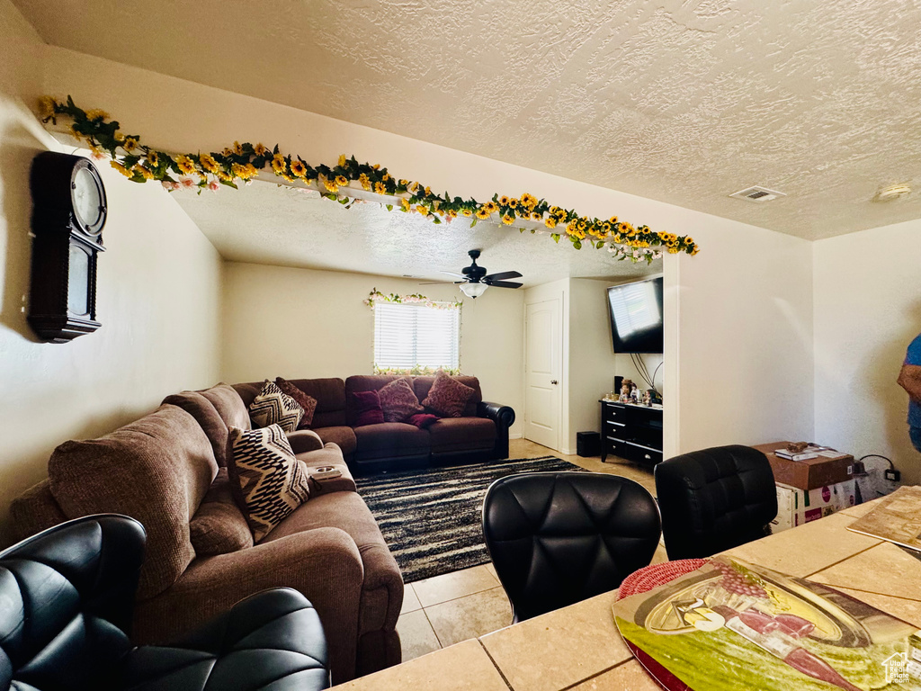 Living area with a textured ceiling, light tile patterned floors, and a ceiling fan