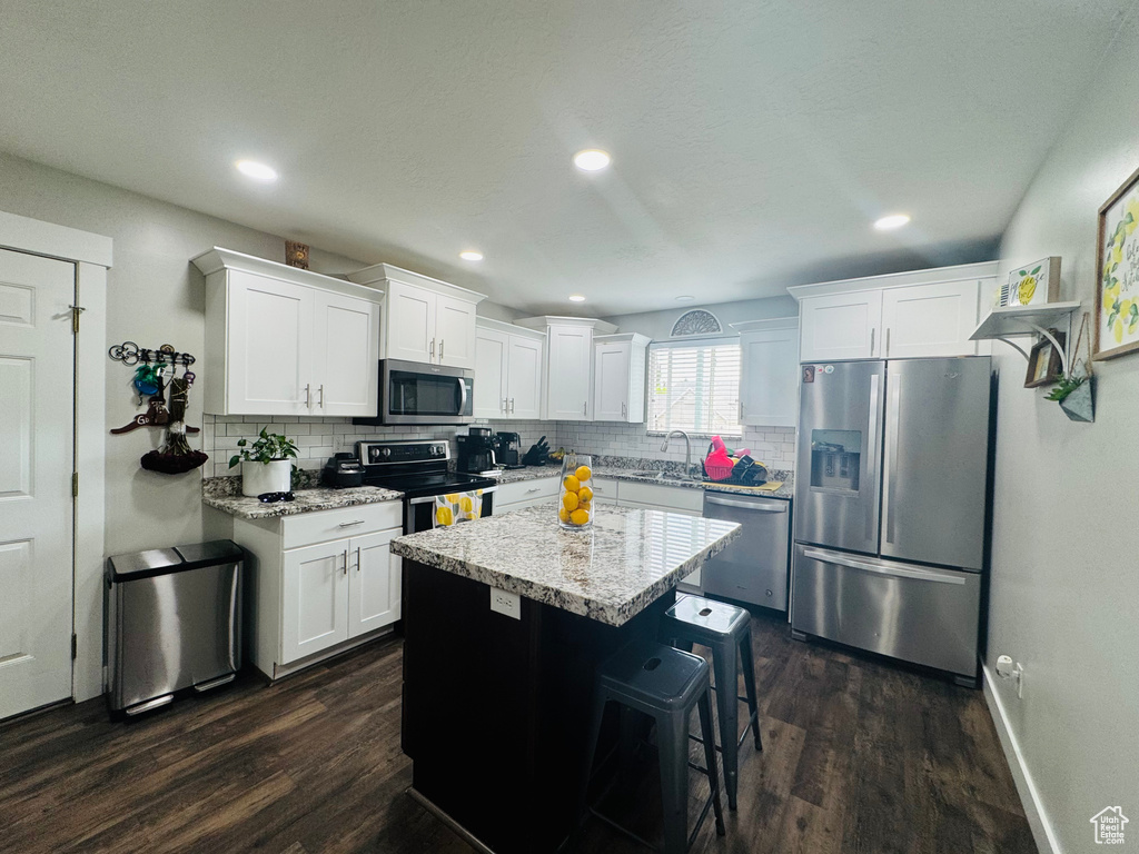 Kitchen featuring stainless steel appliances, a sink, backsplash, dark wood-style flooring, and white cabinets