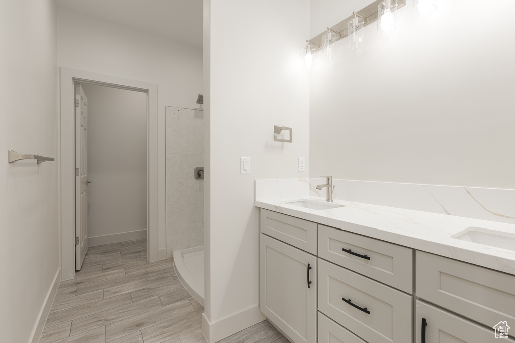 Bathroom with tiled shower, double vanity, wood finished floors, and baseboards