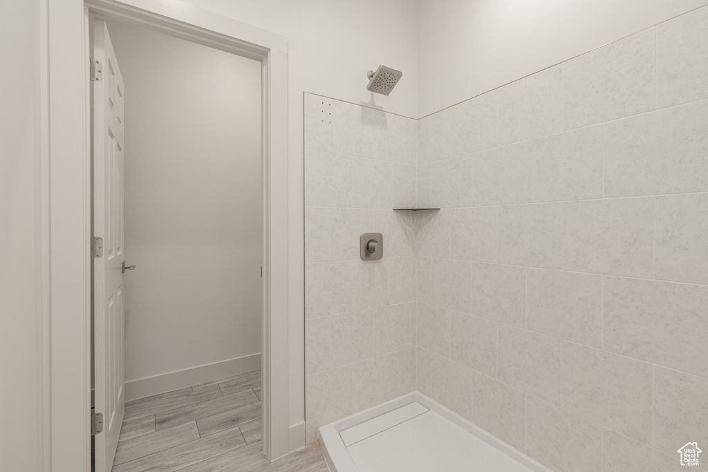Full bath featuring a tile shower, baseboards, and wood finished floors