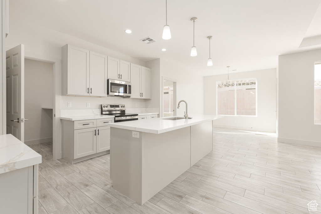 Kitchen with appliances with stainless steel finishes, a sink, a kitchen island with sink, baseboards, and recessed lighting