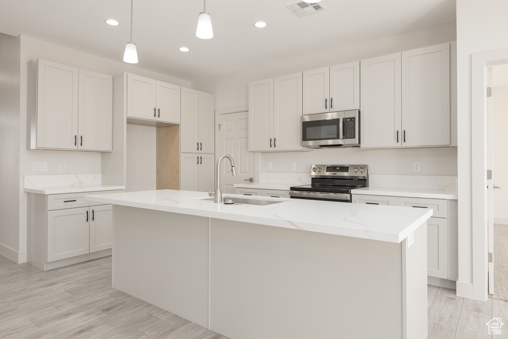 Kitchen with appliances with stainless steel finishes, a sink, recessed lighting, light stone counters, and decorative light fixtures