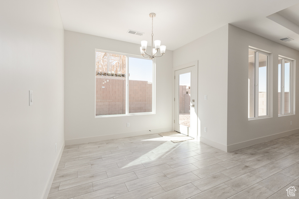 Spare room with a chandelier, light wood finished floors, and baseboards