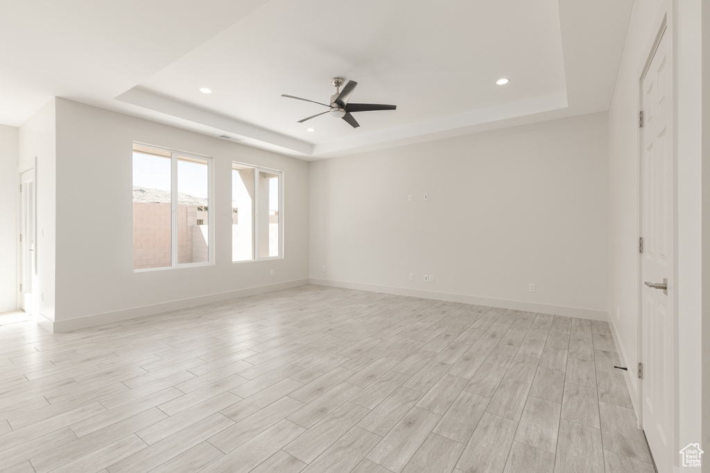 Empty room featuring a tray ceiling, ceiling fan, light wood-style flooring, recessed lighting, and baseboards