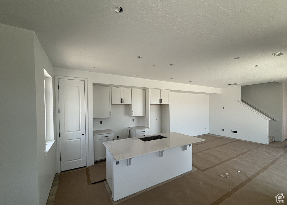 Kitchen featuring a center island with sink, white cabinetry, a breakfast bar, and a textured ceiling