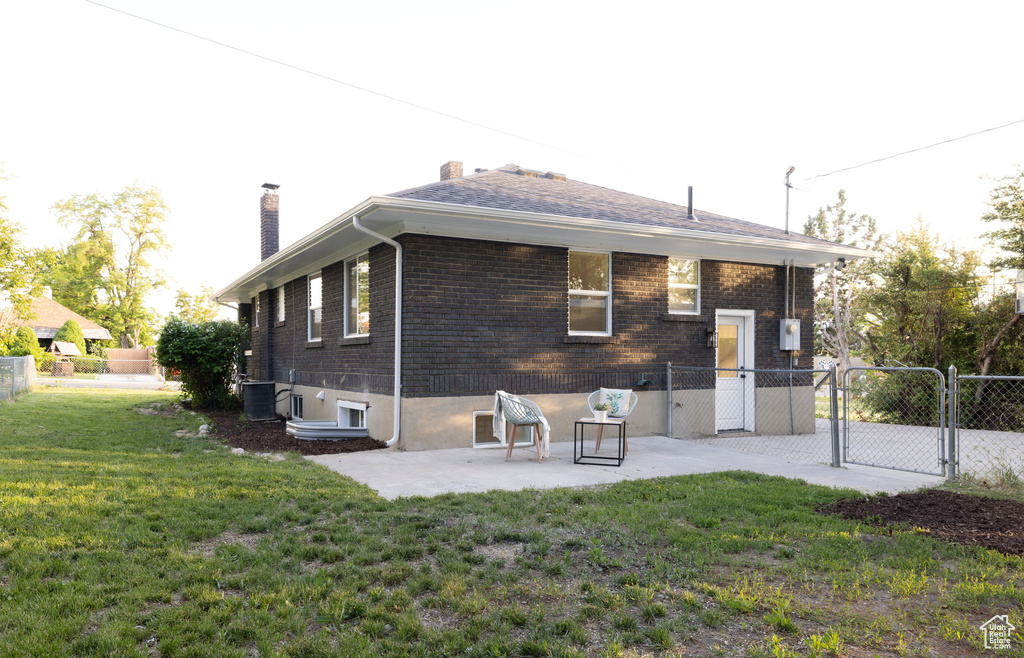 Rear view of house featuring a gate, a chimney, a patio, brick siding, and central AC