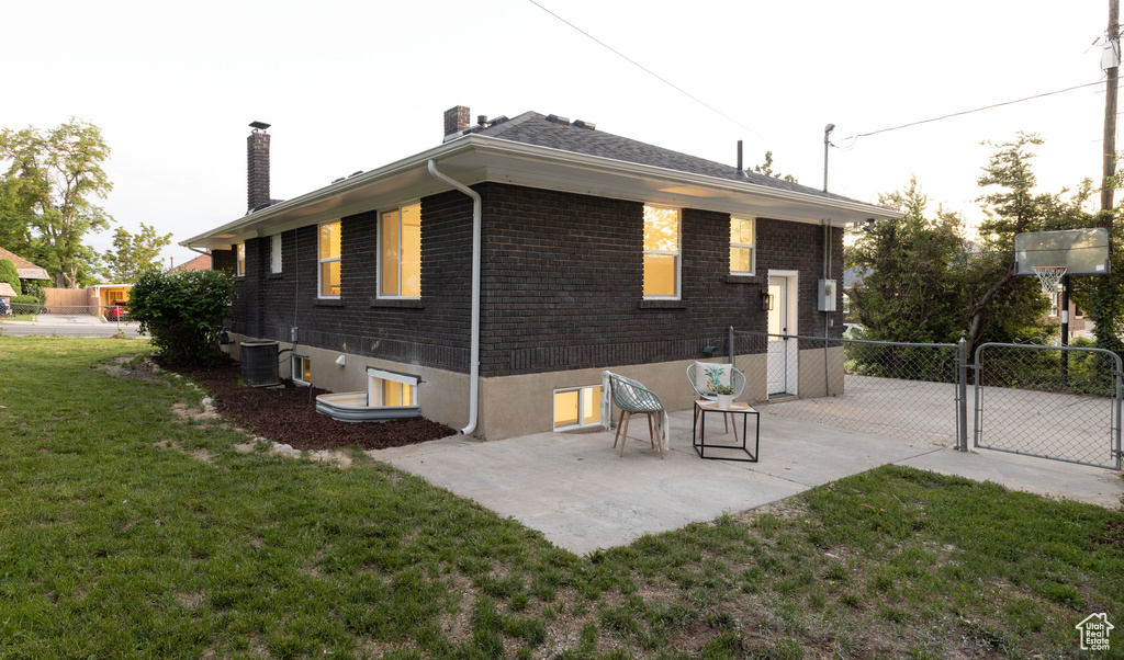 Back of house with a chimney, a gate, central AC unit, brick siding, and a patio area