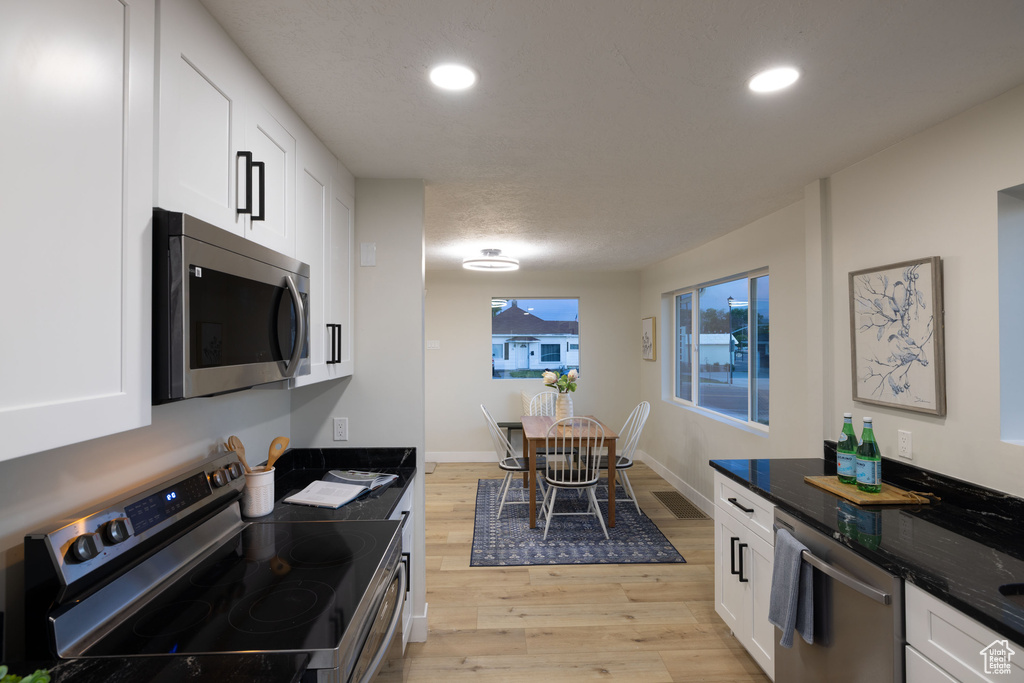 Kitchen with stainless steel appliances, light wood-type flooring, white cabinetry, recessed lighting, and dark stone countertops