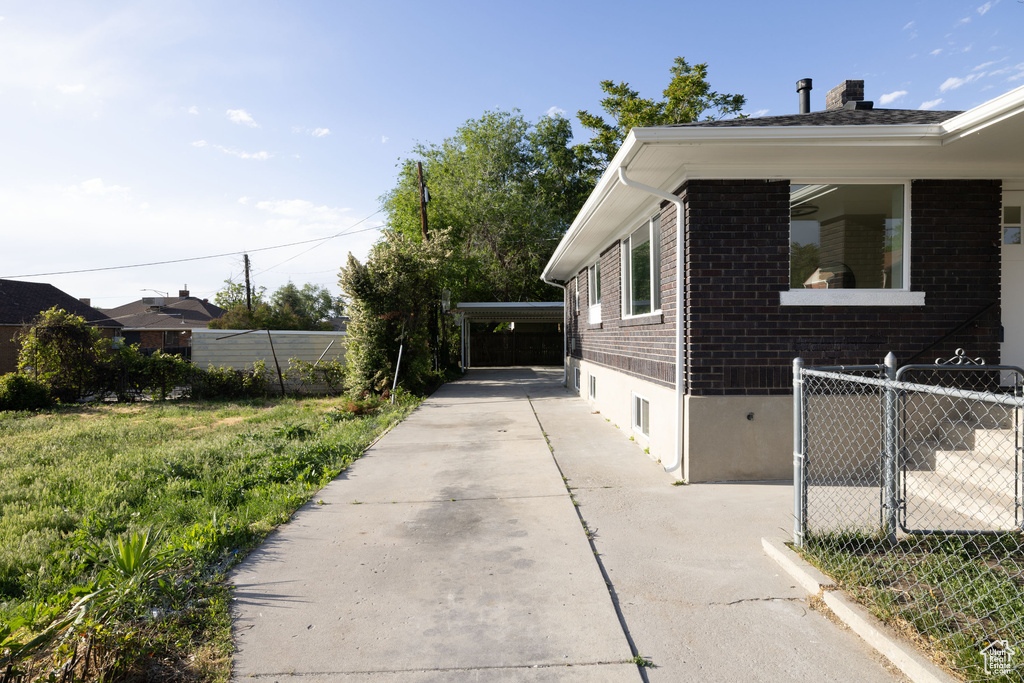 View of side of home with brick siding, driveway, a chimney, and a carport