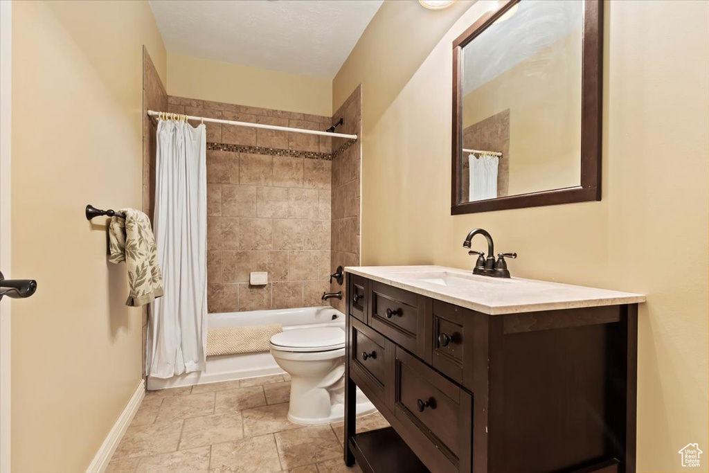 Full bathroom featuring vanity, toilet, baseboards, shower / tub combo with curtain, and stone finish floors