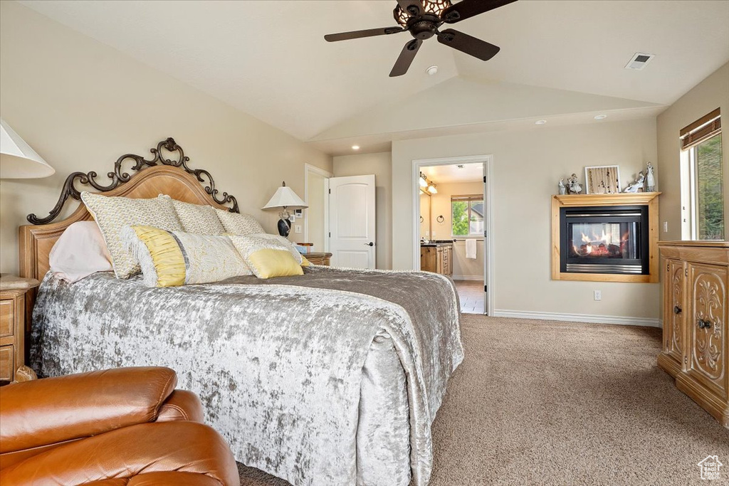 Carpeted bedroom featuring lofted ceiling, a multi sided fireplace, multiple windows, baseboards, and ensuite bathroom