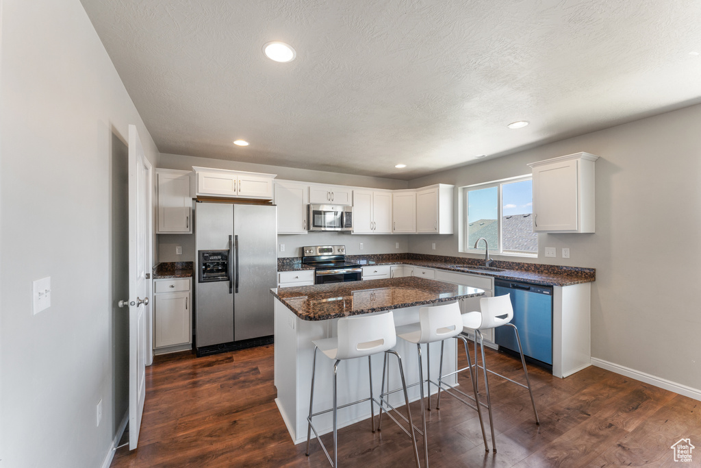 Kitchen featuring stainless steel appliances, a sink, white cabinetry, a breakfast bar, and dark wood-style floors