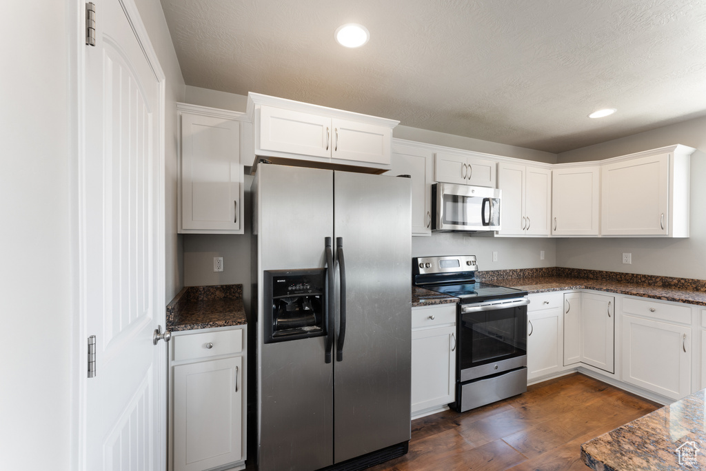 Kitchen with appliances with stainless steel finishes, white cabinets, dark wood-style flooring, dark stone counters, and recessed lighting