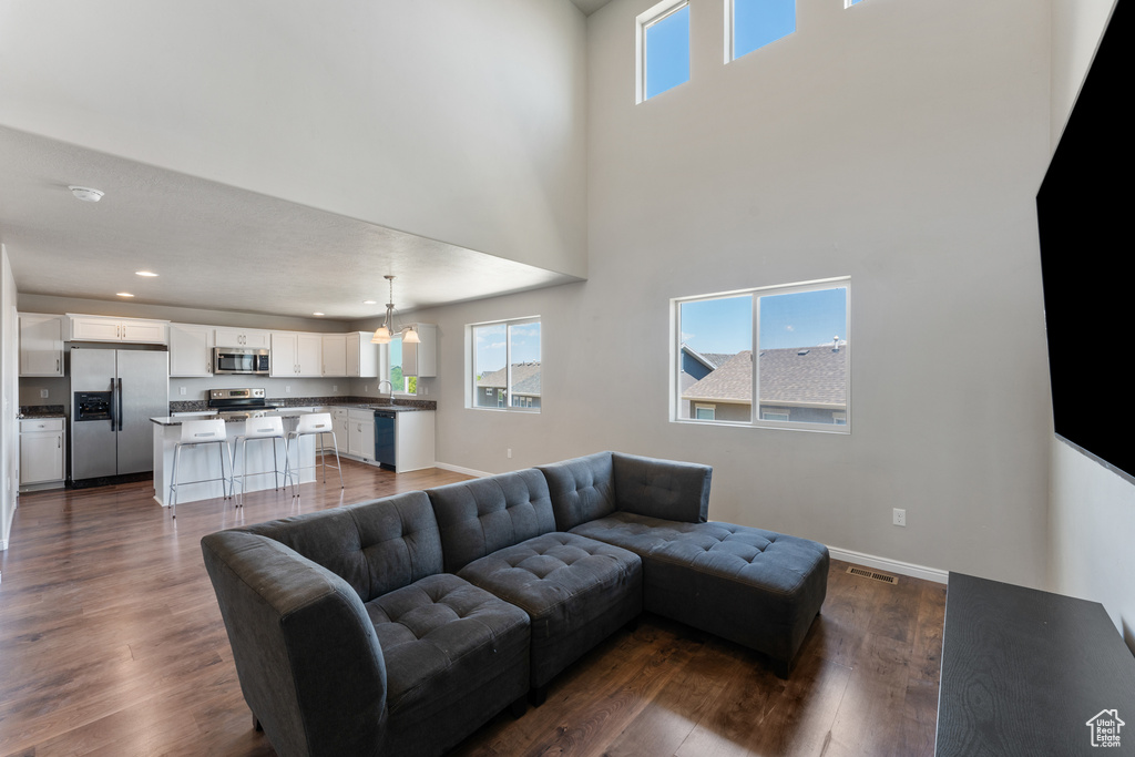 Living area with healthy amount of natural light, dark wood finished floors, baseboards, a chandelier, and a high ceiling
