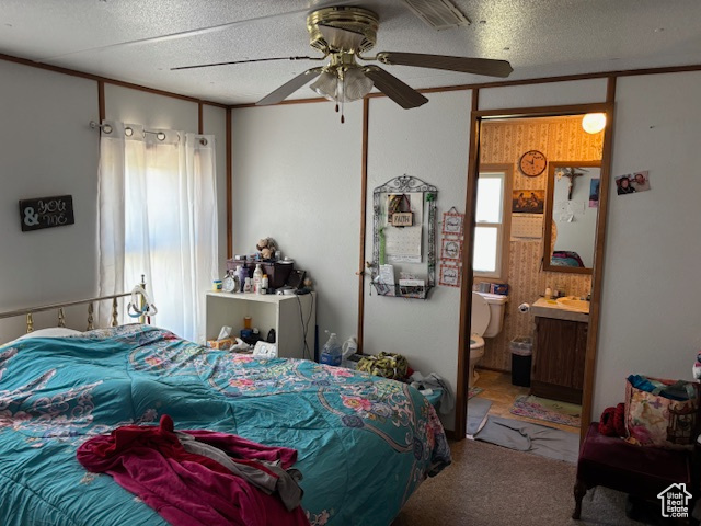 Carpeted bedroom with a textured ceiling, connected bathroom, and a ceiling fan